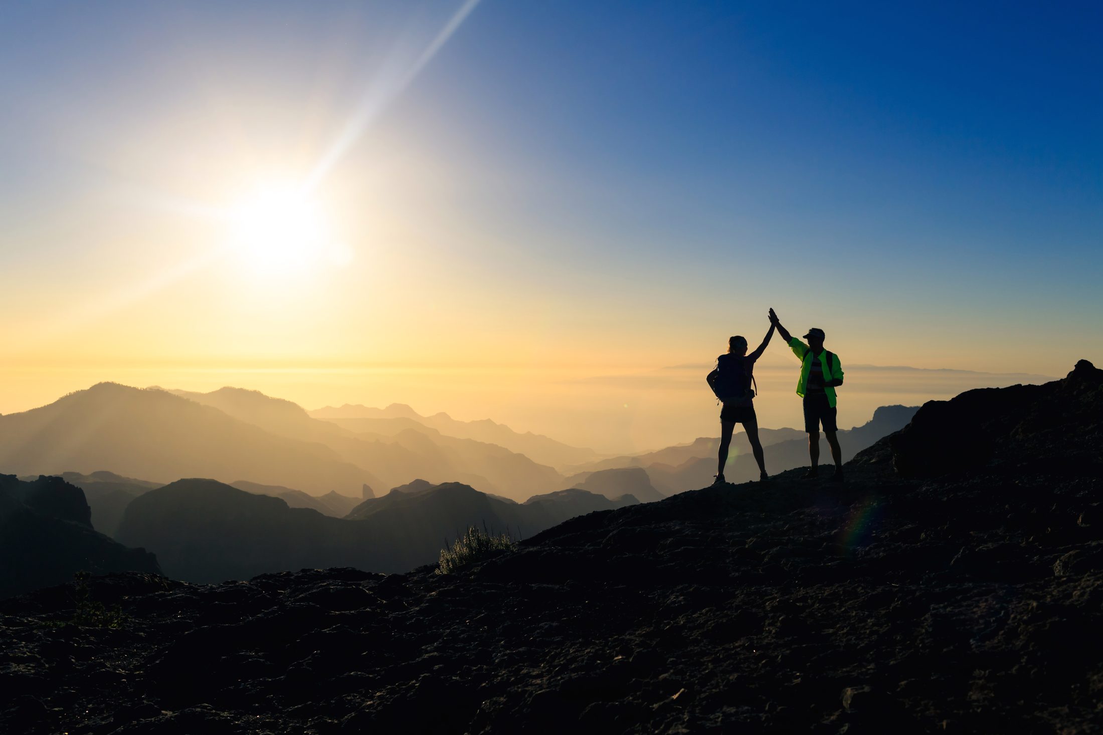 Zwei Wanderer klatschen sich auf einem Bergrücken bei Sonnenaufgang ab